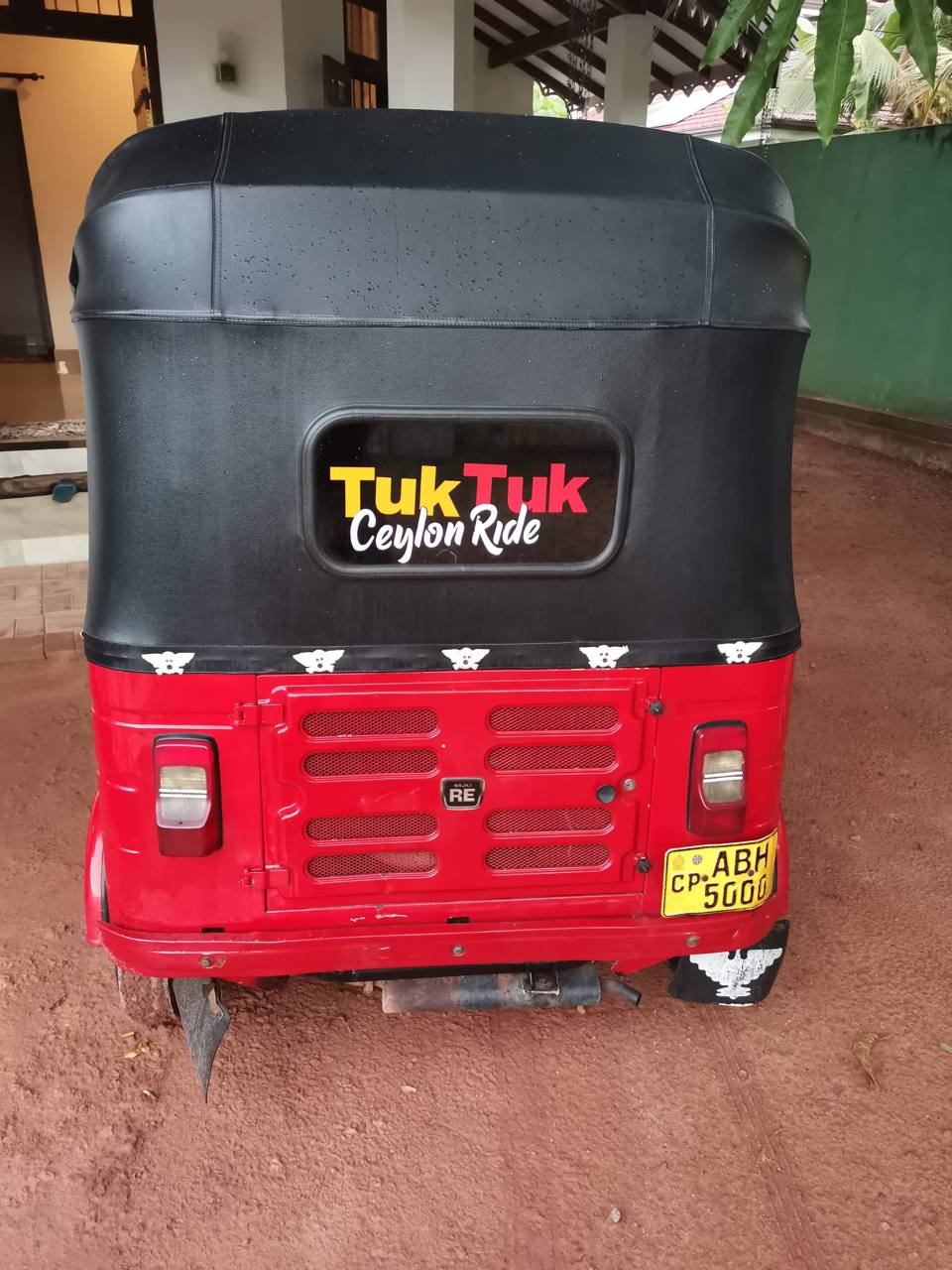 Rückansicht eines roten Tuk-Tuks mit schwarzem Verdeck und Gepäck im Innenraum.