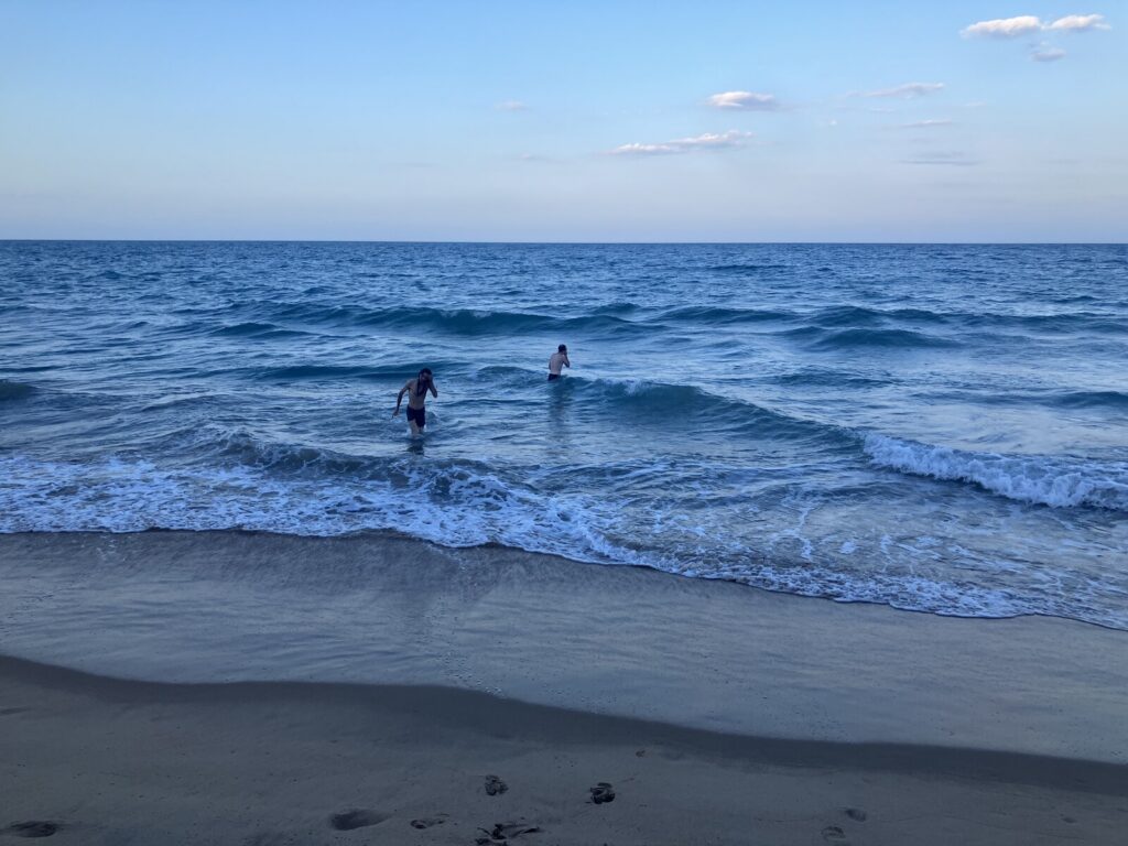 Zwei Männer im Meer in der Abenddämmerung, das Wasser wirkt kühl und blau.