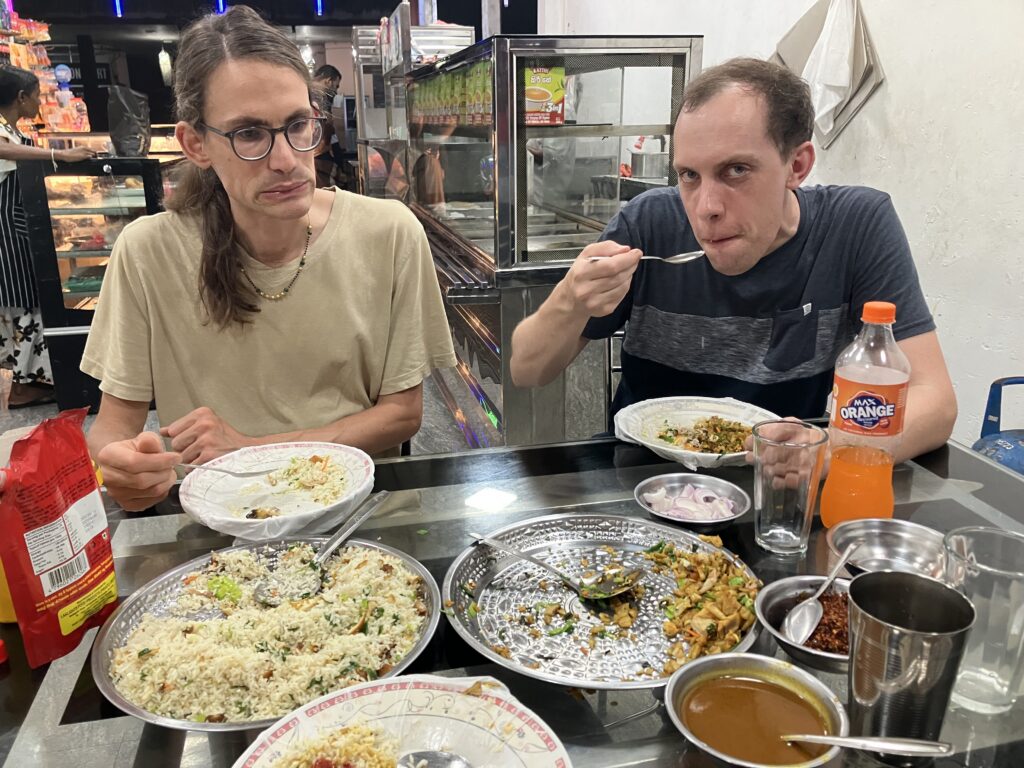 Zwei Männer an einem Edelstahltisch mit Reis, Currysoße und Zwiebelringen.